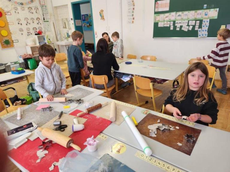 Kinder in einem Klassenraum, auf den Tischen liegen Backutensilien und ausgestochene Teigfiguren.