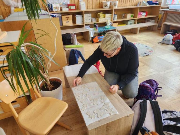 Person kniet an einem Holztisch und arbeitet an ausgestochenen Teigformen