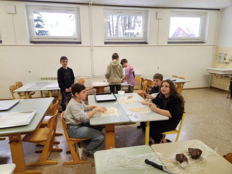 Mehrere Kinder in einem hellen Klassenraum bearbeiten Teig