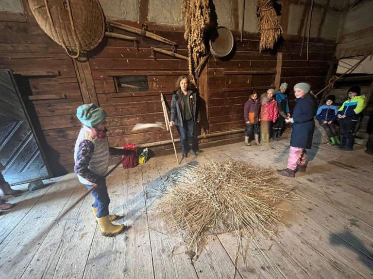 Mehrere Kinder auf einer Tenne, zwei dreschen Getreide