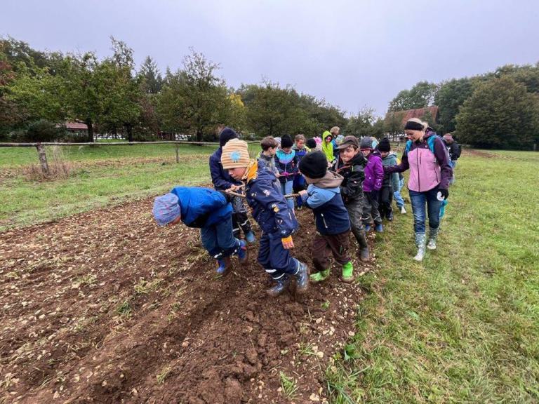 Eine Gruppe von Kindern ziehein eine Egge über einen Acker