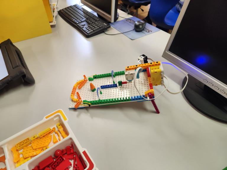 Roboterkonstruktion aus bunten LEGO-Teilen auf einem Schreibtisch neben Tastatur und Monitor.
