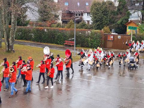 Musiker in roten Oberteilen und Narren mit Masken laufen über den Schulhof
