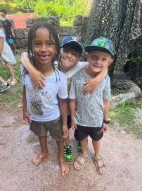 Gruppe von lächelnden Kindern, die vor einer steinernen Mauer im Freien posieren.