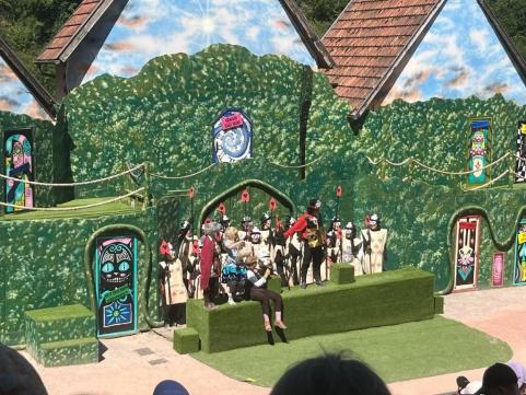 Ein detaillierter Theateraufbau mit grüner Kulisse und kostümierten Figuren in einer märchenhaften Szene.