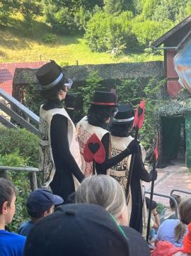 Schauspieler in auffälligen Kostümen im Freien vor einer grünen Kulisse.